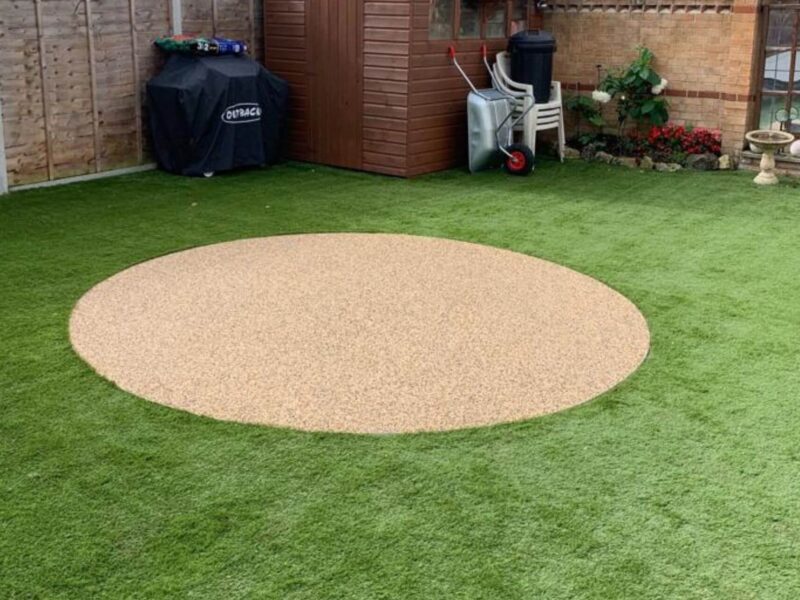 Circular resin bound patio in golden aggregate surrounded by artificial grass lawn