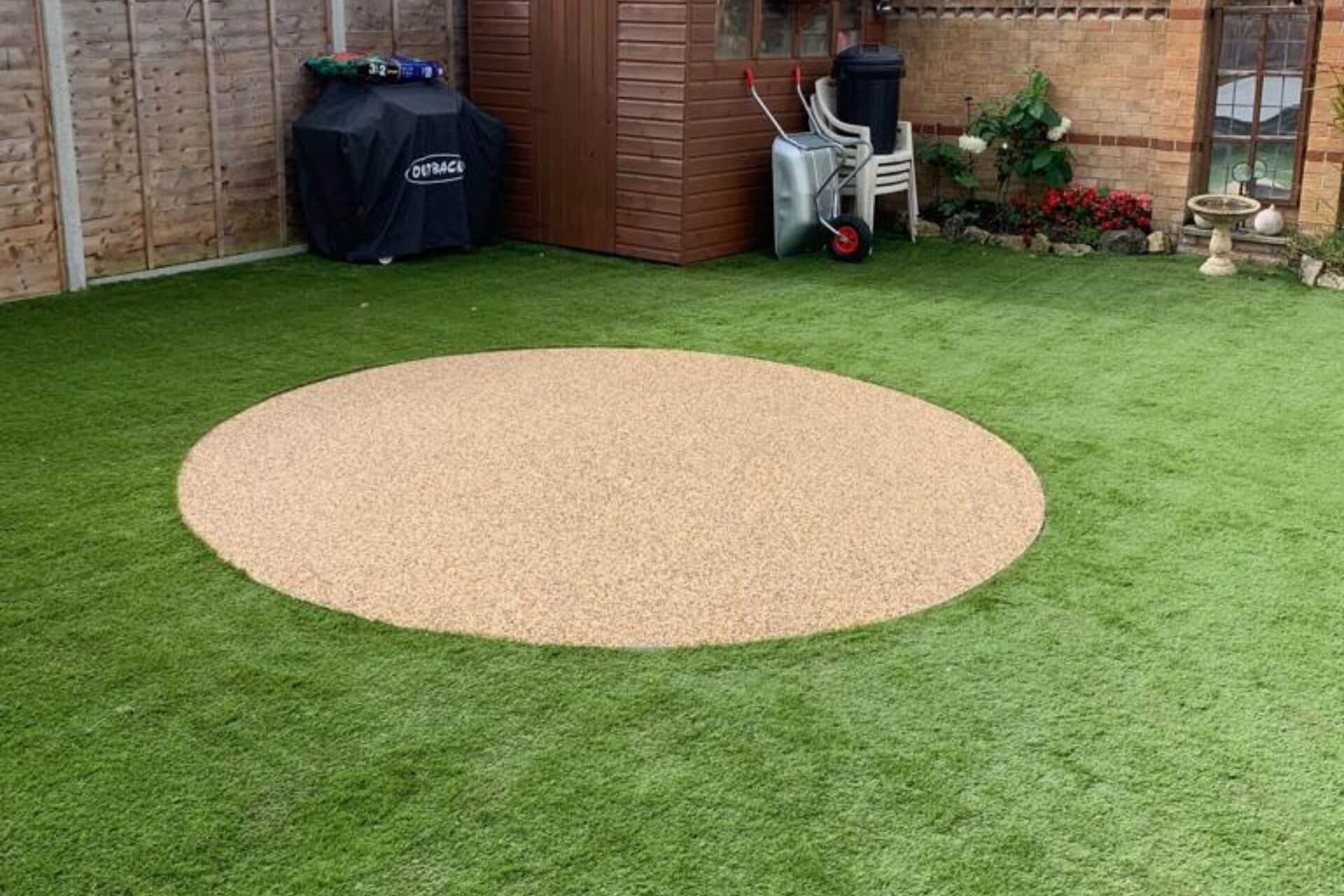Circular resin bound patio in golden aggregate surrounded by artificial grass lawn