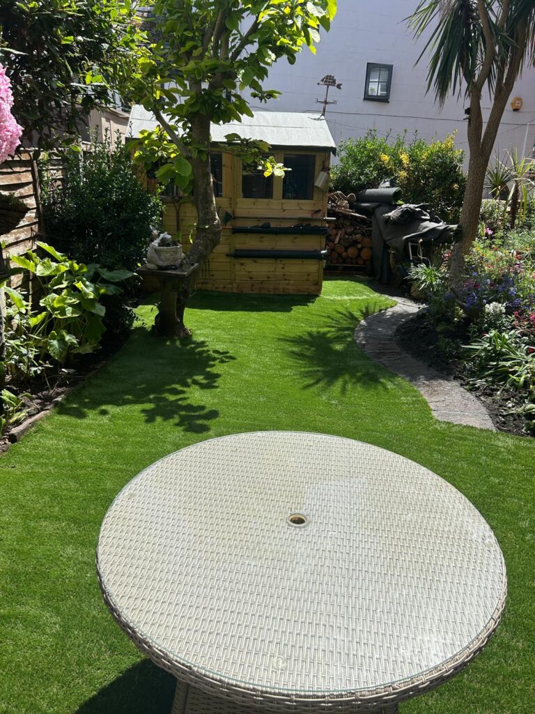 Artificial grass lawn leading to a timber summerhouse in a narrow rear garden, Teignmouth
